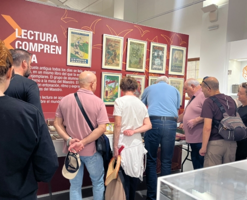 Visitantes reunidos ante el panel Lectura comprensiva, con portadas enmarcadas de antiguos libros escolares de lectura, mientras exploran los objetos de la mesa.