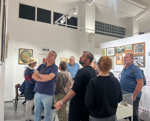 Grupo de visitantes atendiendo a las explicaciones del director en la sala dedicada a la escuela, junto a fotografías antiguas de aulas.